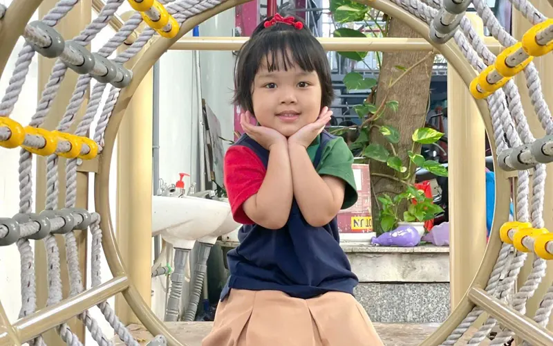 A smiling girl in uniform poses inside a rope ring on the climbing frame