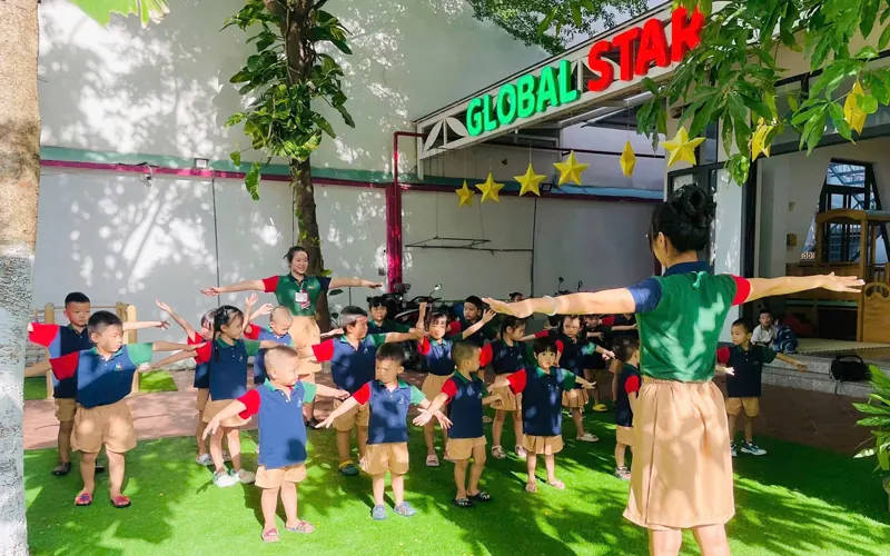 Children stretch their arms wide with a teacher on the green play yard